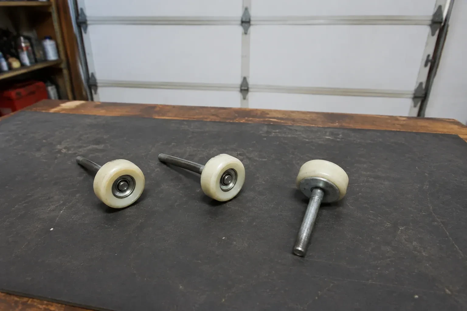 Three detached nylon-wheel garage door rollers with steel stems on a work mat. — Garage Door Roller Replacement, Hamilton