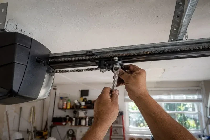Hands holding a wrench against an opener trolley beneath a chain rail — Chain-Drive Opener Repair, Hamilton