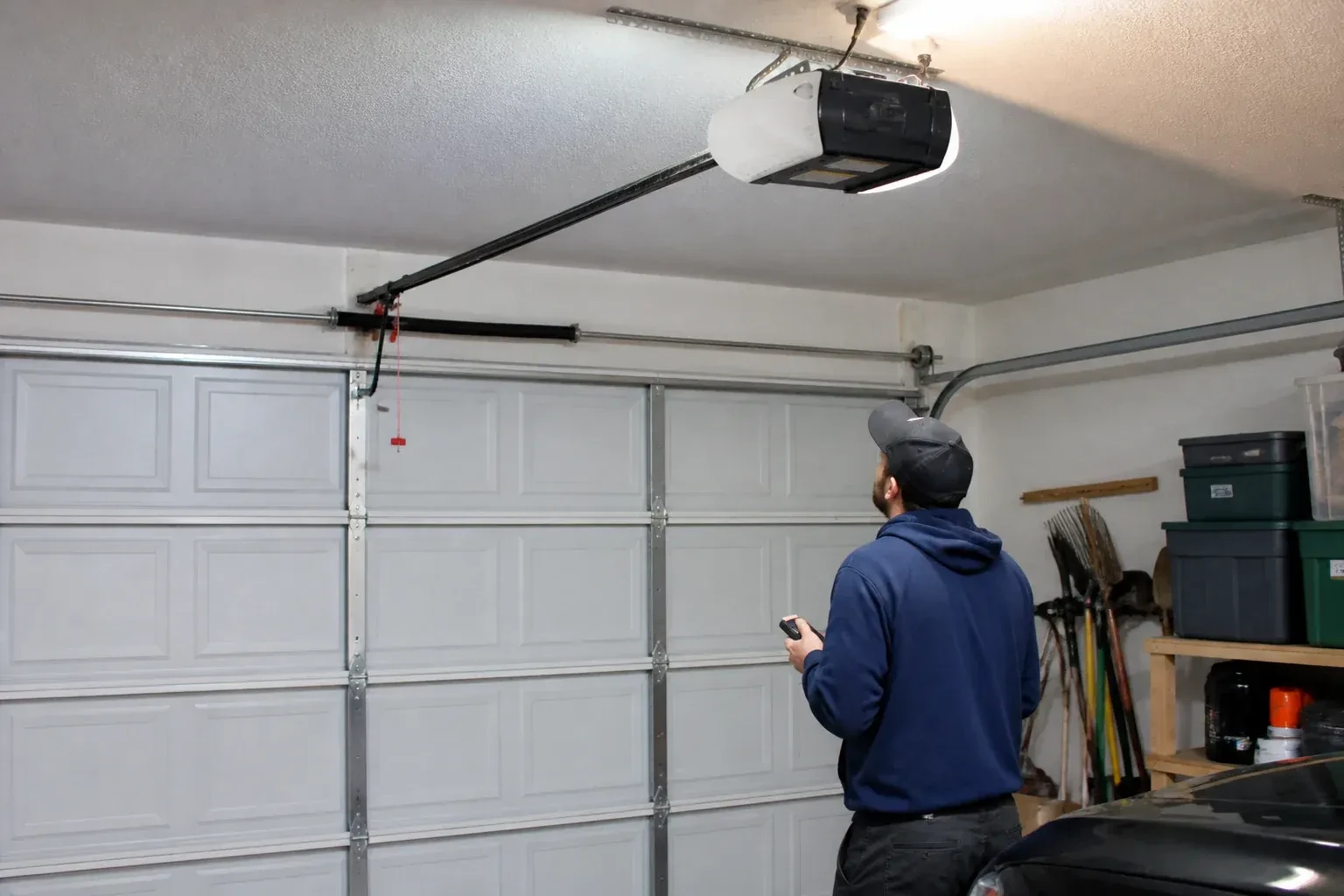 A person holding a remote looks toward an overhead garage-door opener and rail. — Garage Door Opener Diagnosis and Repair, Hamilton