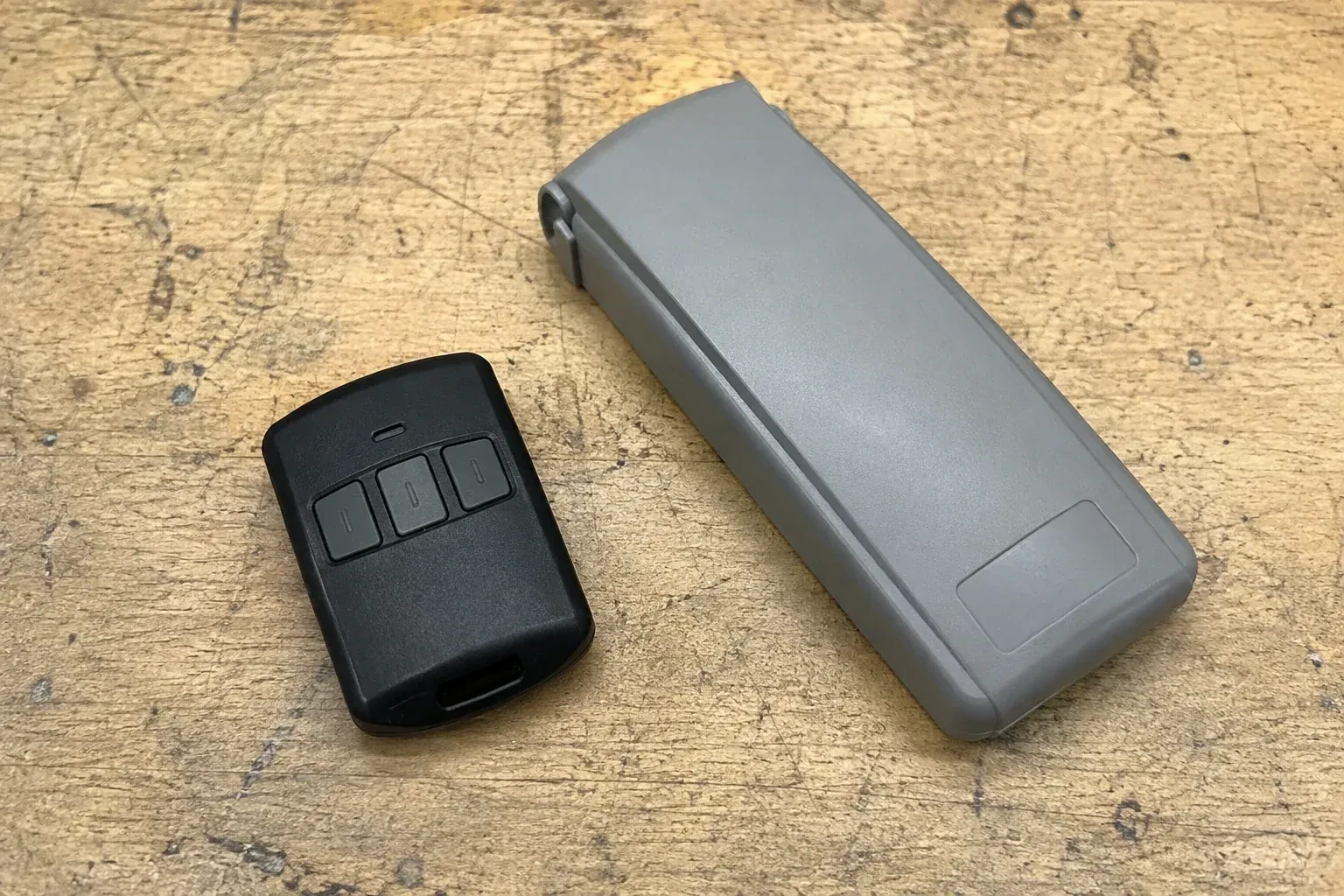 Three-button remote beside a closed grey keypad cover on a workbench. — Garage Door Remote and Keypad Programming, Hamilton